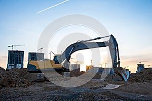 Excavator during earthmoving at construction site on sunset background. Ð¡onstruction machinery for excavating. Tower cranes