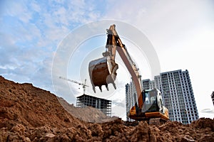 Excavator during earthmoving at construction site on sunset background. Ð¡onstruction machinery for excavating. Tower cranes