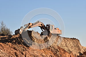 Excavator during earthmoving at open pit on blue sky background. Construction machinery and earth-moving heavy equipment for