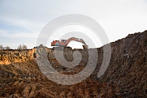 Excavator during earthmoving work at open-pit mining on blue sky background. Loader machine with bucket in sand quarry