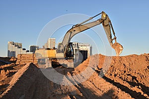 Excavator on earthworks at construction site. Backhoe on foundation work and road construction. Tower cranes in action on blue sky