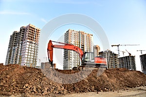 Excavator on earthworks at construction site. Backhoe on foundation work and road construction. Tower cranes in action on blue sky