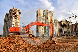 Excavator during excavation at construction site on sunset background. Red Backhoe on road work. Heavy Construction Equipment for
