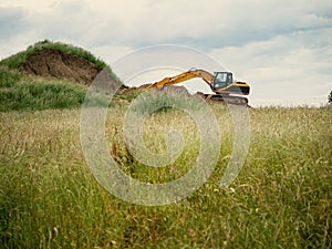 Excavator in a field digging out a hill, cloudy sky, Concept construction site, land development, heavy industry