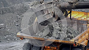 Excavator fills dump truck. Bucket excavator closeup loads stones into body of dump truck on mining or construction of