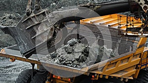 Excavator fills dump truck. Bucket excavator closeup loads stones into body of dump truck on mining or construction of