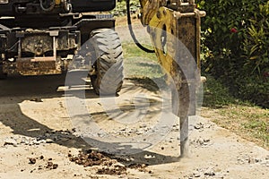 An excavator fitted with a hydraulic breaker destroying a portion of a damaged street. Road demolition in progress