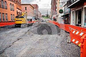 excavator on a gravel road during road work on the street between tall buildings