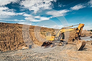 Excavator with heavy duty scoop moving earth and loading dumper trucks during roadworks at highway construction