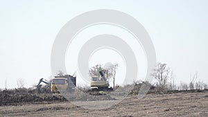 Excavator on the horizon is dumping dirt into the dump truck, field