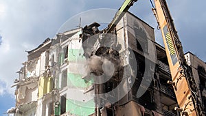 Excavator with hydraulic crusher at the demolition of a residential building. City renewal. Dismantling, destruction of a high-