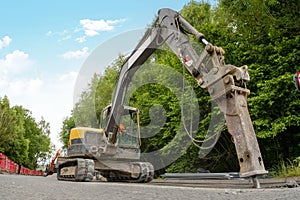 Excavator with hydraulic jack hammer breaking asphalt in preparation for drainage works close up