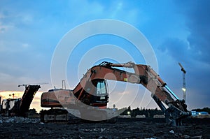 Excavator with hydraulic shears at construction site against the background sunset. Road repair, Demolition work concrete,