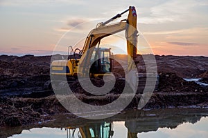 Excavator at lake in the quarry on sunset background. Backhoe during earthmoving work at open-pit mining. Earth-moving