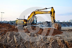 Excavator with a large iron bucket on a construction site during road works. Backhoe dig the ground for the foundation, laying