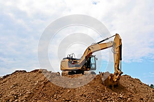 Excavator on large pile of dirt with blue sky