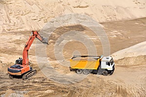Excavator load the sand to the heavy dump truck in the open-pit. Heavy machinery working in the mining quarry. Digging and