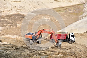 Excavator load the sand to the heavy dump truck in the open-pit. Heavy machinery working in the mining quarry. Digging and