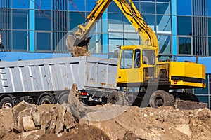 Excavator loader and dump truck during earthworks at a construction site. Loading land in the back of a heavy truck.