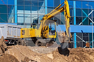 Excavator loader and dump truck during earthworks at a construction site. Loading land in the back of a heavy truck.