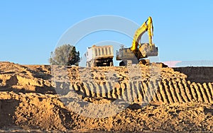 Excavator loader with rised backhoe and a truck in a sky background