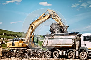 excavator loading dumper trucks at garbage dumping site