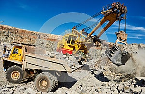 Excavator loading granite or ore into dump truck at opencast