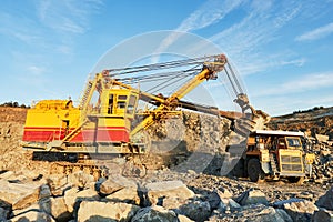 Excavator loading granite or ore into dump truck at opencast