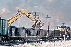 Excavator loading old railroad ties in open boxcars