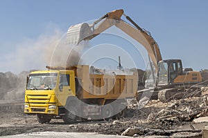 Excavator loading rubble into a dump truck at a construction site