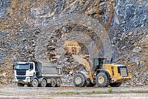 an excavator is loading a truck with stone at a quarry