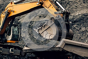 Excavator loads coal into the back of a heavy mining dump truck.