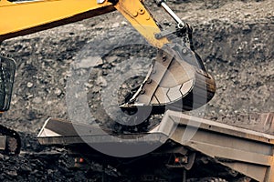 Excavator loads coal into the back of a heavy mining dump truck.