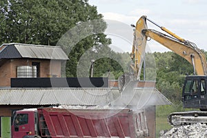 Excavator loads construction waste into a red truck. Destroyed concrete, construction waste.