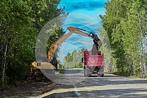 Excavator loads dump truck with earth during roadworks to deepen storm drain.