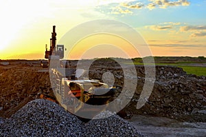 Excavator in a mining quarry at sunset. Mobile Stone crusher machine by the construction site or open pit for crushing concrete