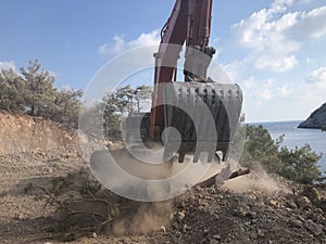 Excavator moving soil with lots of dust during excavation works on the rocky soils. Heavy machinery at earthmoving