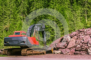 Excavator and pile of stones near forest