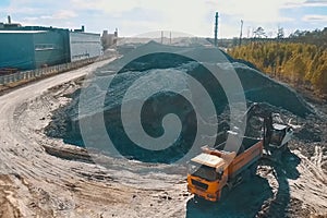 An excavator pours clay into dump truck for brick production