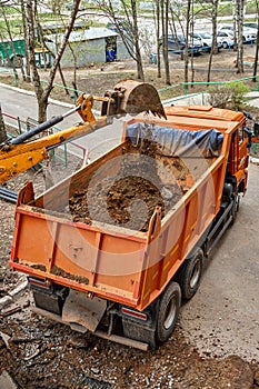 Excavator pours dirt into bodywork of tipper truck in yard