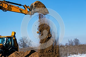 The excavator in the process of work digs out the earth and pours it onto the site.