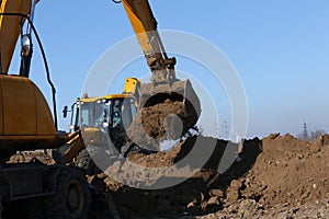 The excavator in the process of work digs out the earth and pours it onto the site.
