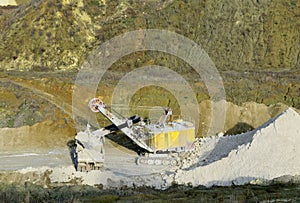 Excavator in quarry loads rock into a mining truck. Excavators and trucks work in a chalk open pit. Aerial top view of mining