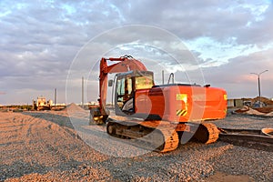 Excavator during road work at construction site on awesome sunset background. Screeding gravel for laying asphalt and borders