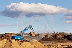 Excavator at sandpit during earthmoving works, in the blue sky