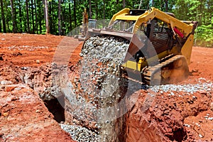 Excavator with scoop on skid-steer loader unloading gravel at construction area outdoors