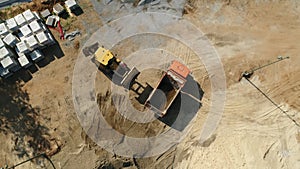 Excavator scoops and fills dump truck bed with moist sand