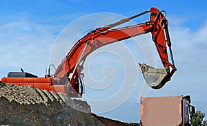 Excavator shovel over a dump truck against blue sky with clouds