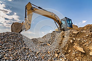Excavator on top of a mountain of stone and sand from a quarry