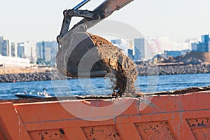 Excavator unloading sand into the dump truck on the construction site, excavating and working during road works, backhoe and